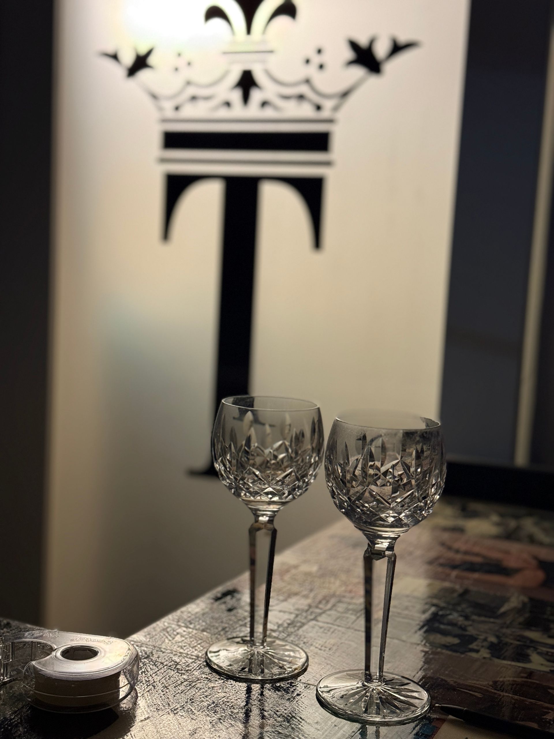 Two ornate wine glasses on a table before a large decorative T