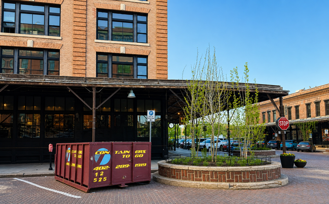 Brick plaza with a planter, maroon storage bins, and a brick building on a sunny day