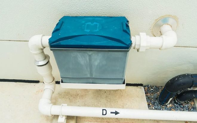 Blue and gray water filter box attached to pipes on a wall.