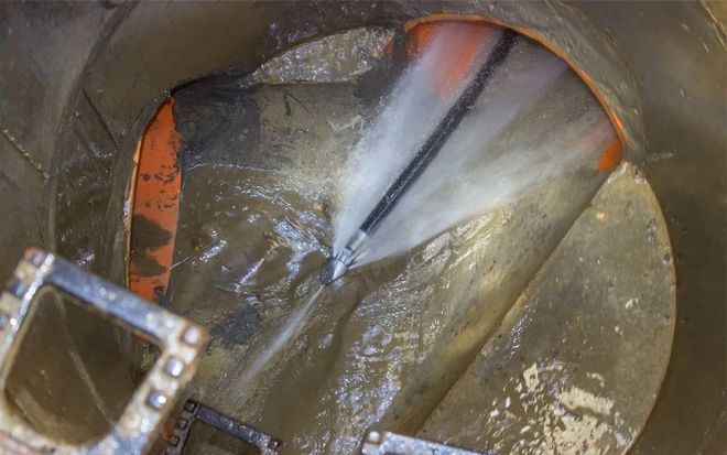 Inside a sewer pipe, a high-pressure jet is cleaning the surface with spraying water.