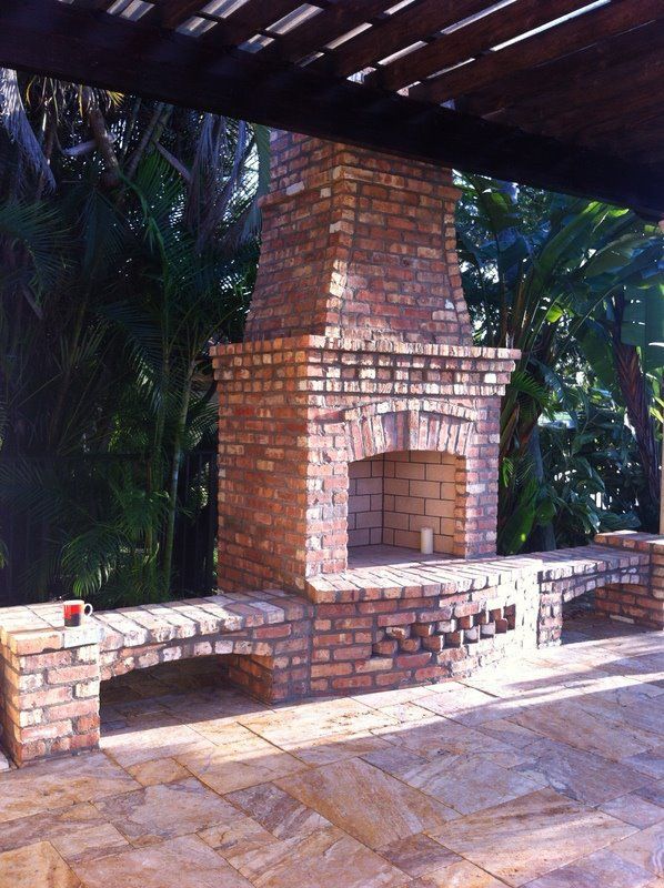 A brick fireplace sits under a wooden pergola