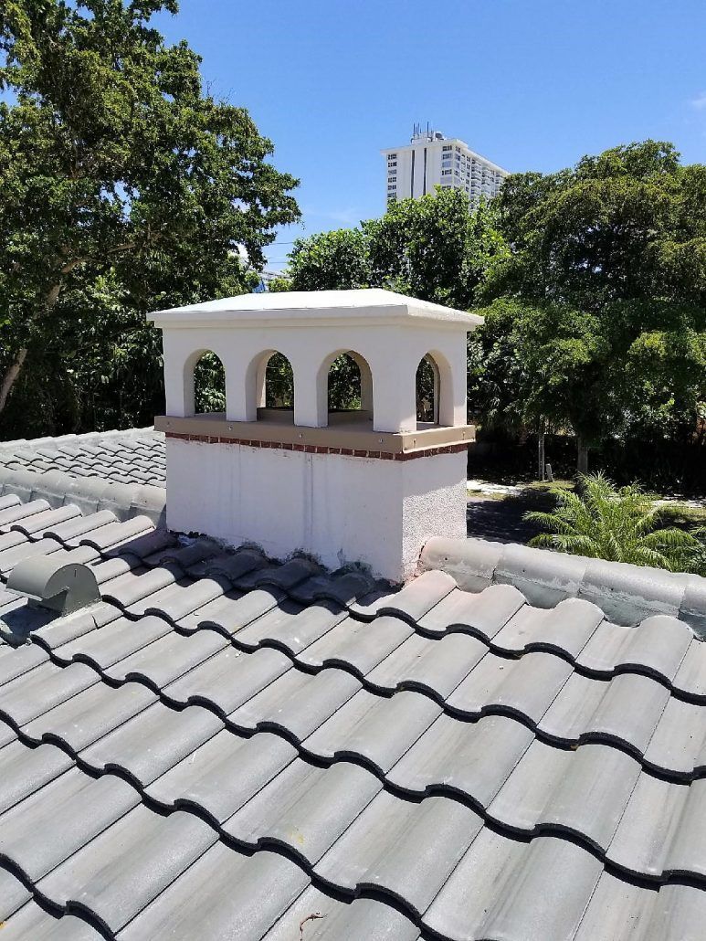 A chimney on top of a tiled roof with trees in the background.