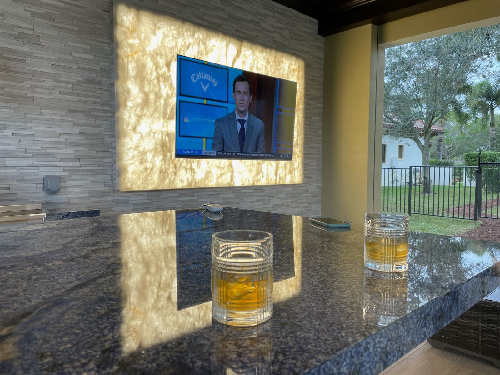 Two glasses of whiskey are on a counter in front of a television.