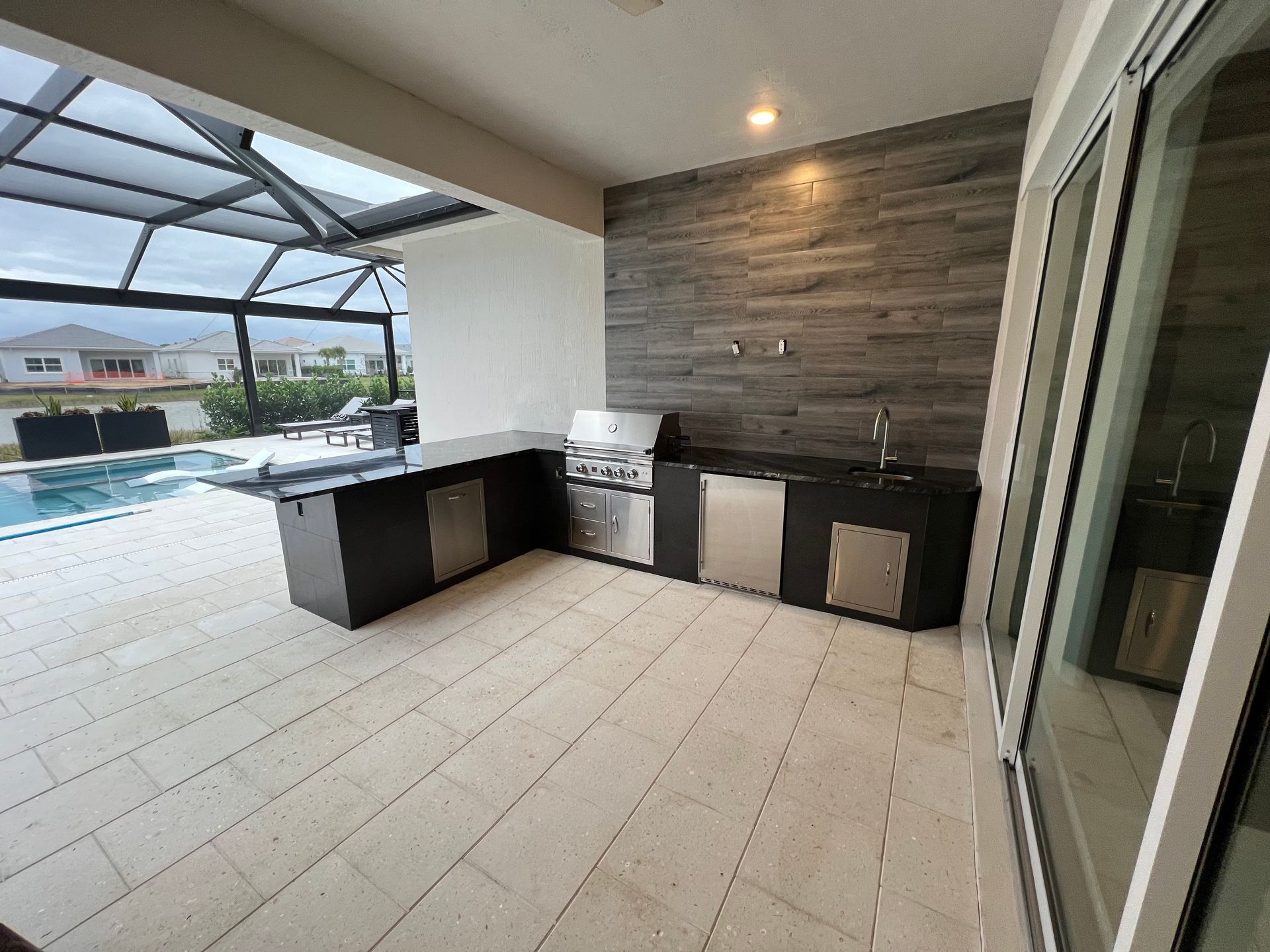 A patio with a grill and a swimming pool in the background.