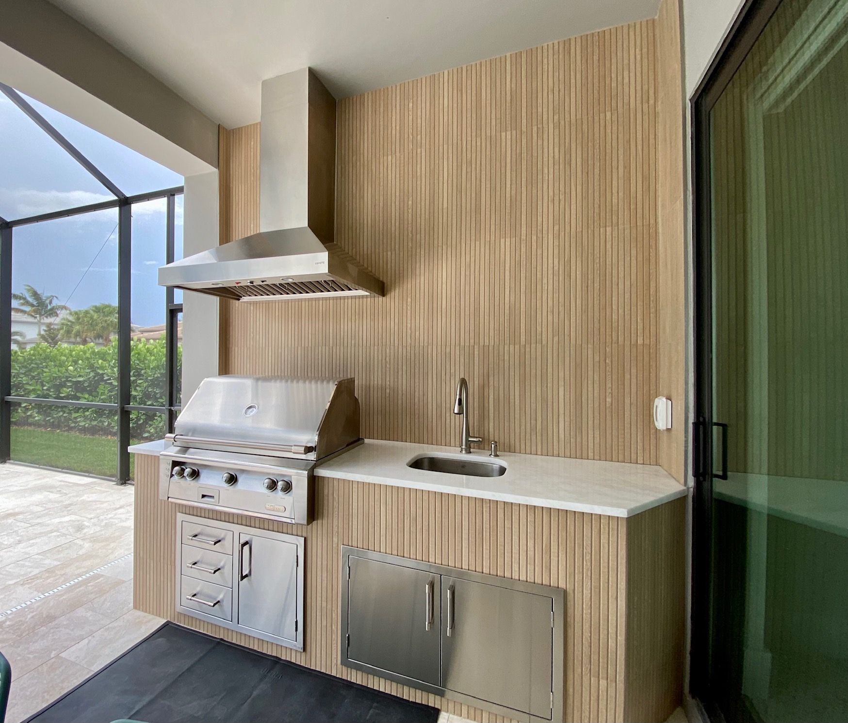 Modern outdoor kitchen with stainless steel grill, hood, and sink in Boca Raton, FL.