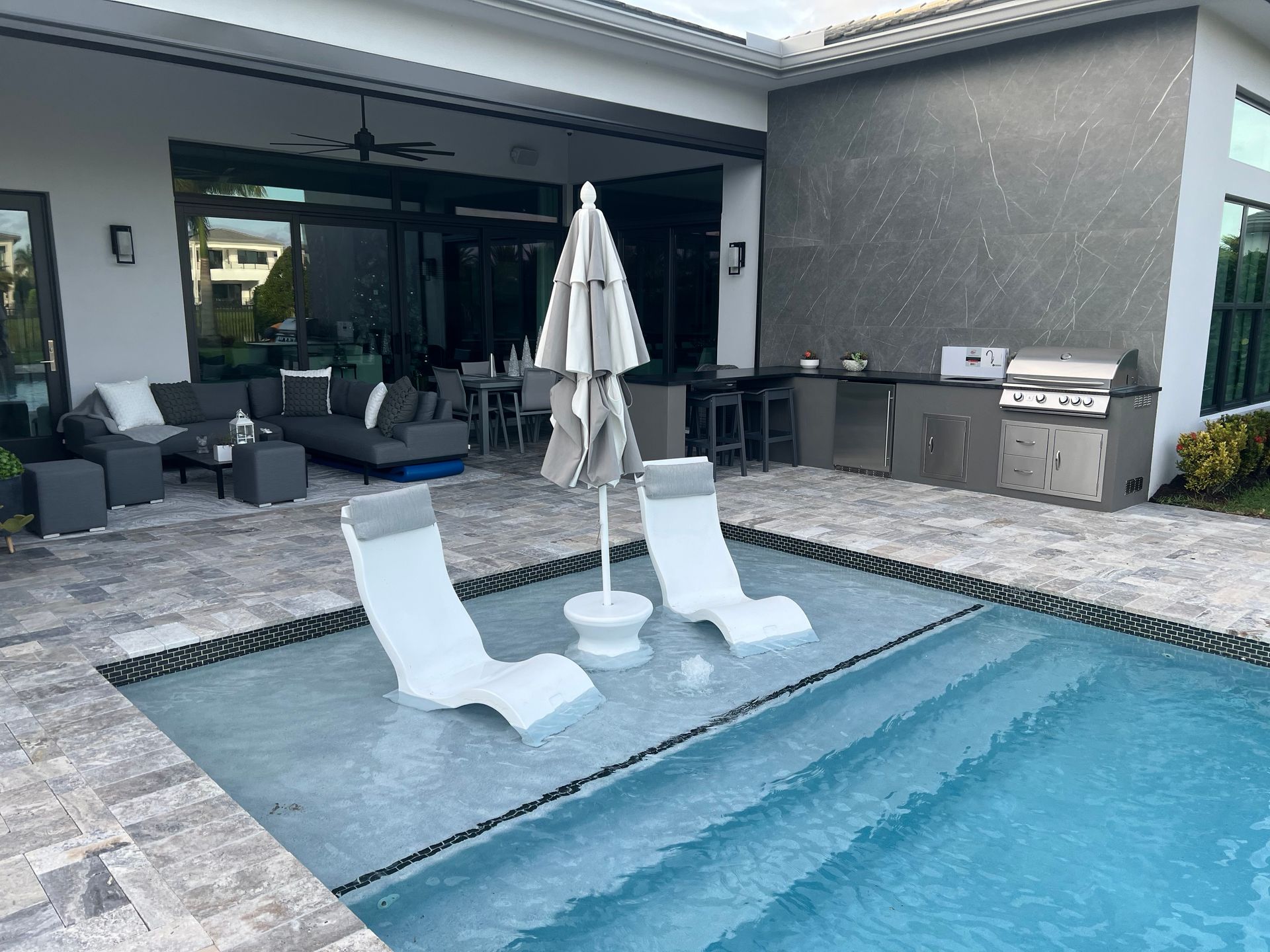 A swimming pool with chairs and umbrellas in front of a house.