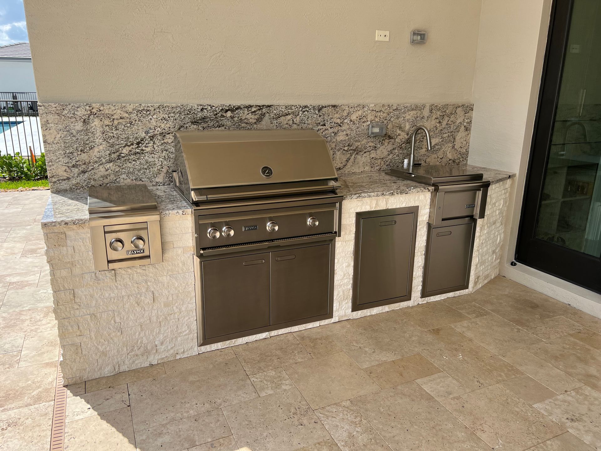 An outdoor kitchen with a grill , sink , and granite counter tops.