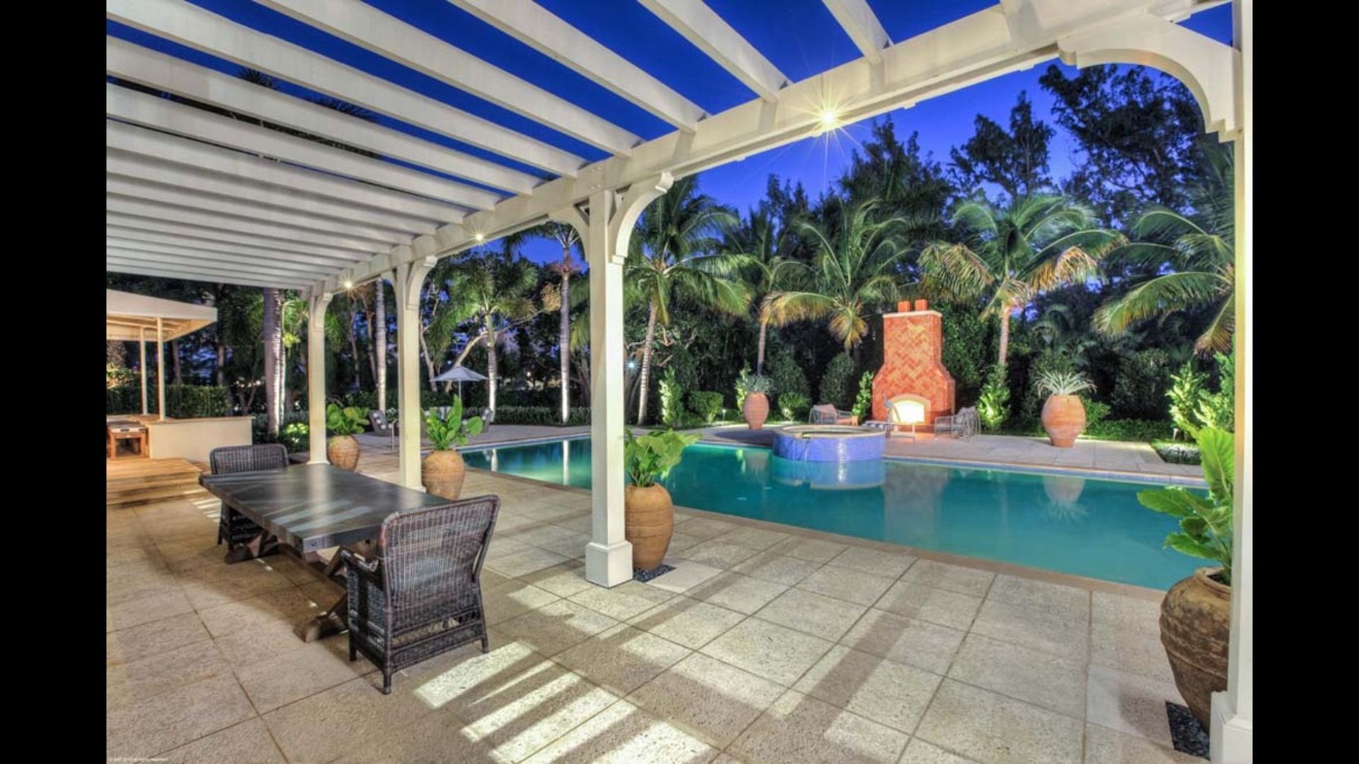 A large swimming pool with a table and chairs under a pergola.