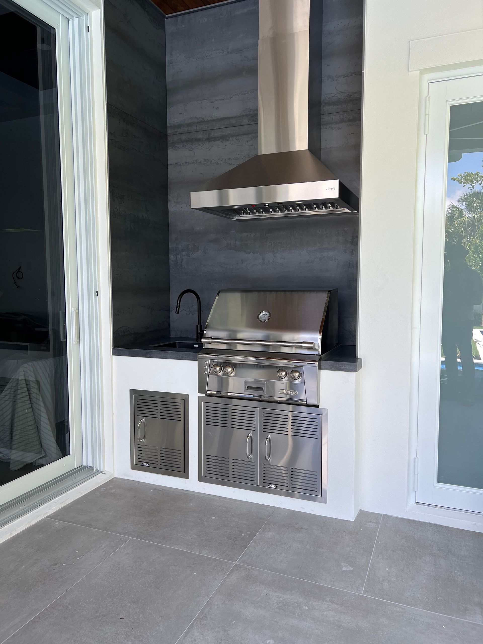 A stainless steel grill is sitting on a patio next to a window.