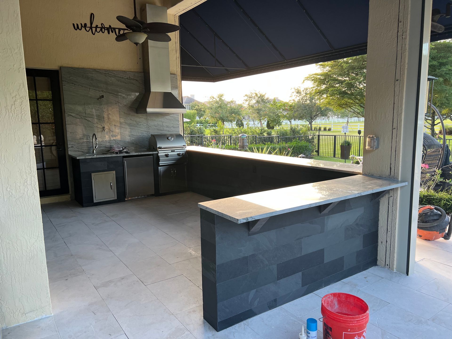 A large outdoor kitchen with a ceiling fan and a bucket of paint.