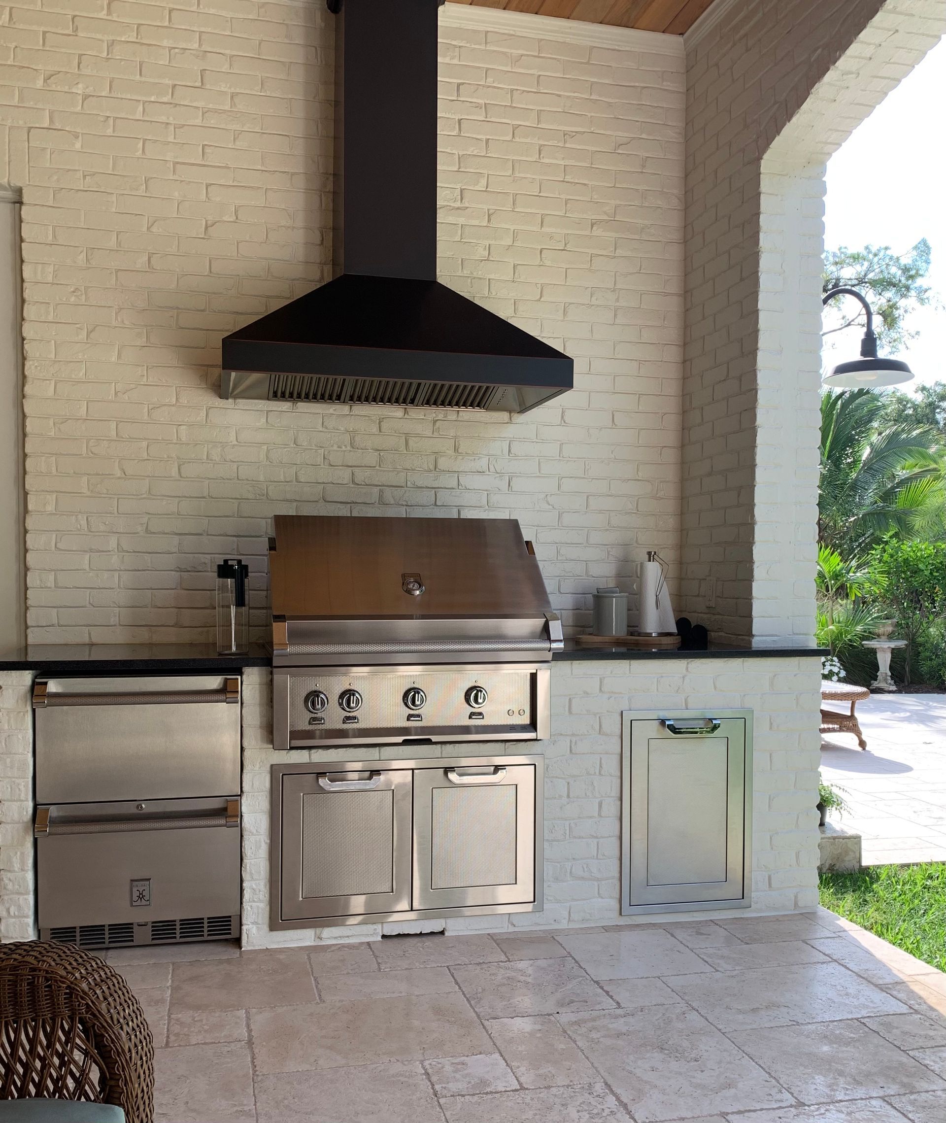An outdoor kitchen with a stainless steel grill and a hood