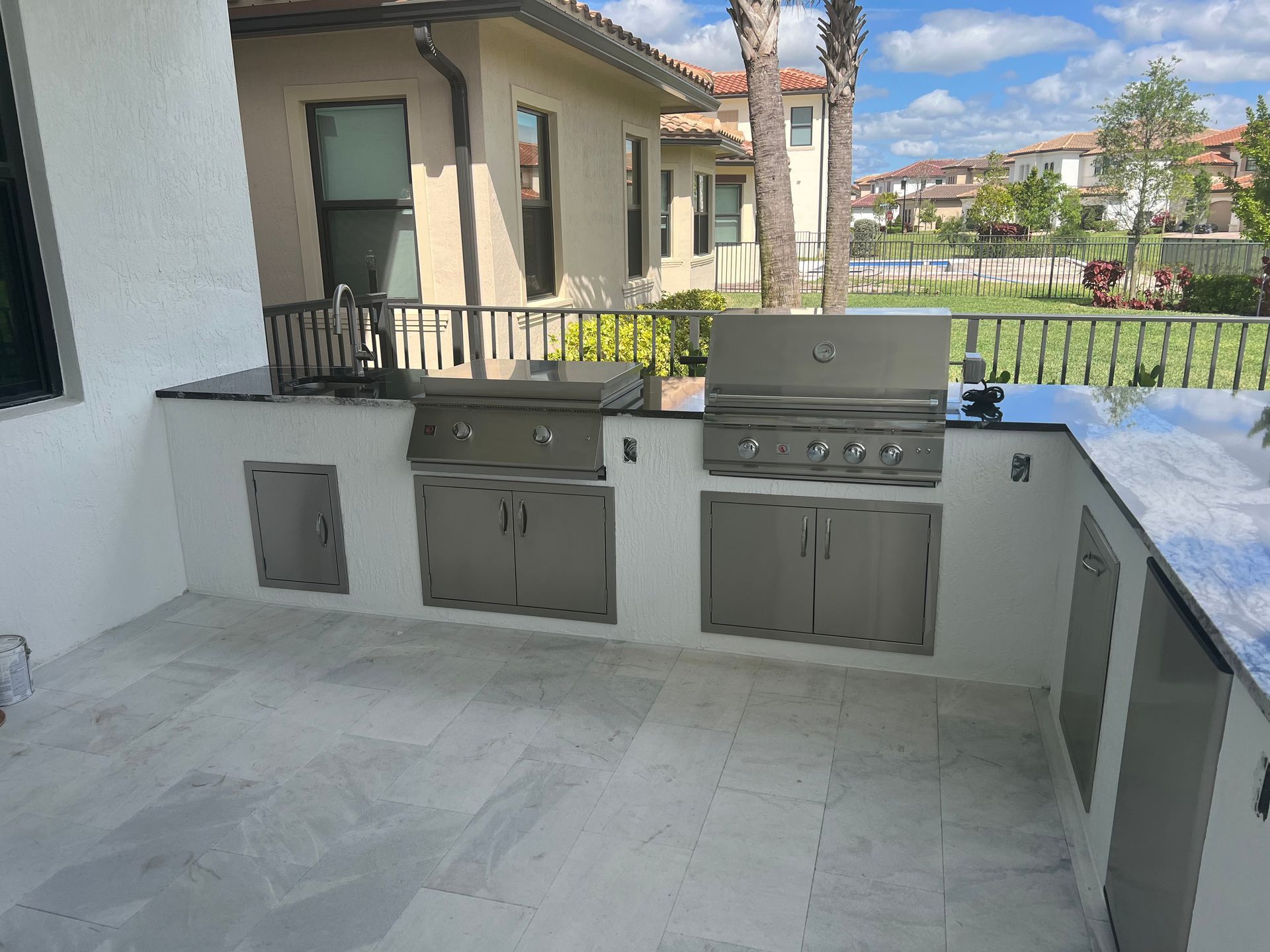A large outdoor kitchen with a grill and stainless steel cabinets.
