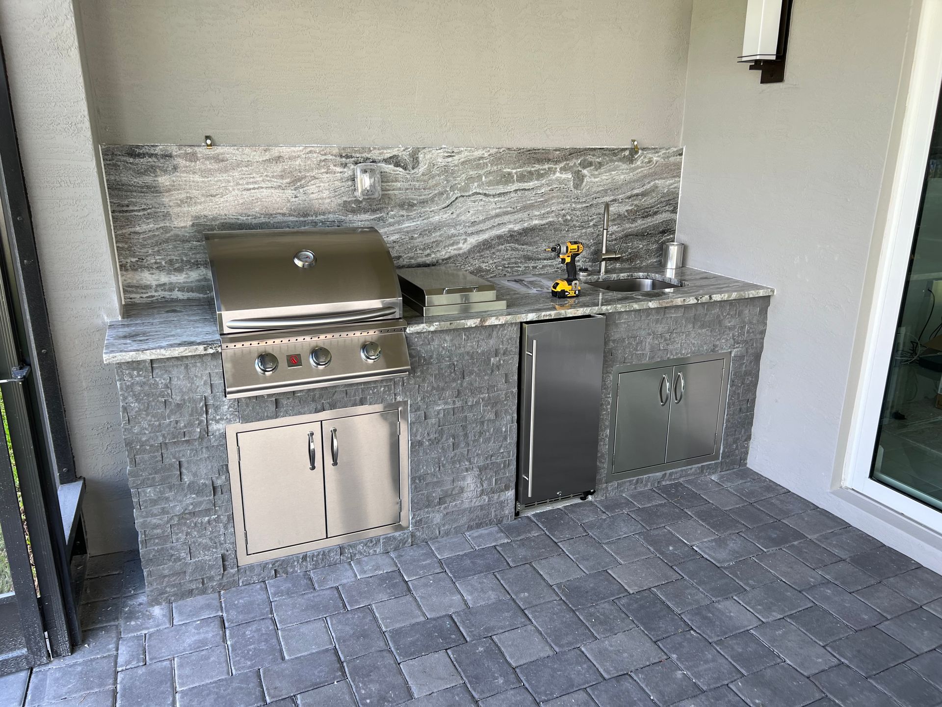 A patio with a grill , sink , and refrigerator.
