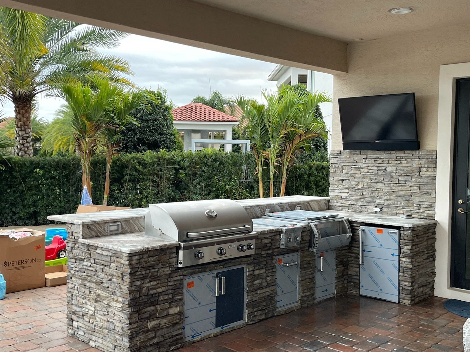 A large outdoor kitchen with a grill , sink , and television.