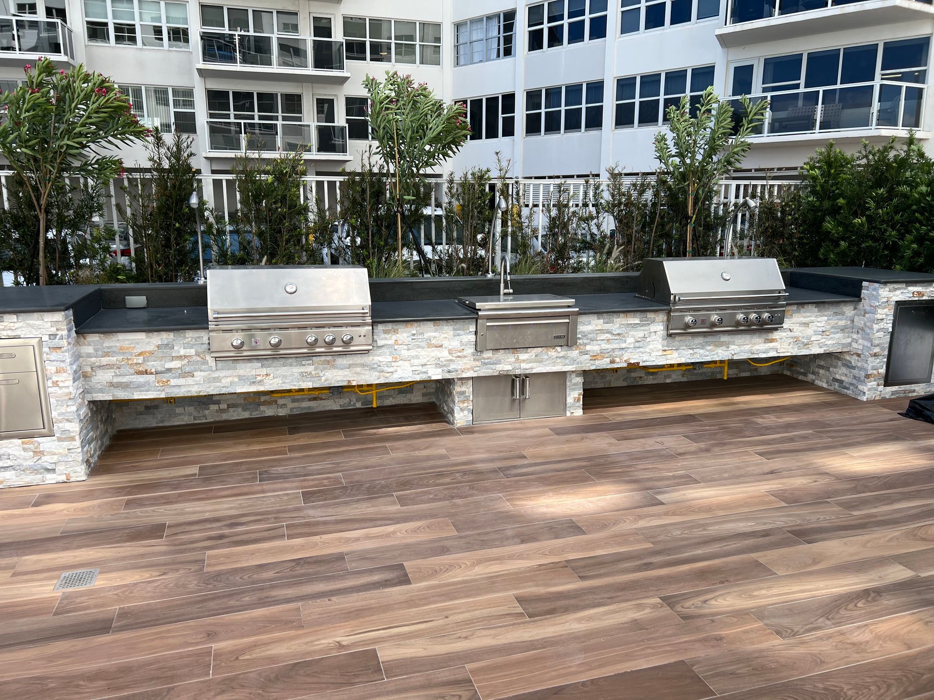 A row of grills are sitting on a wooden deck in front of a building.