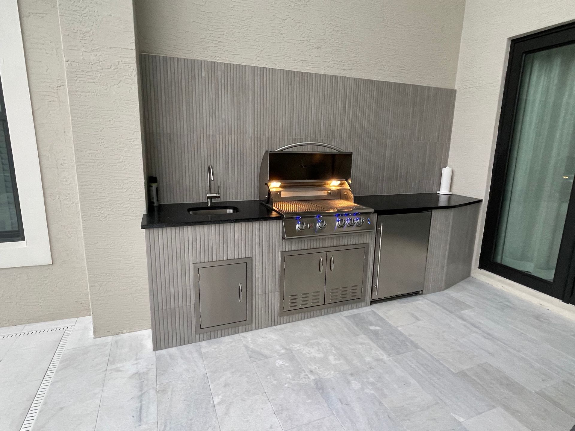 An outdoor kitchen with a grill , sink , and refrigerator.