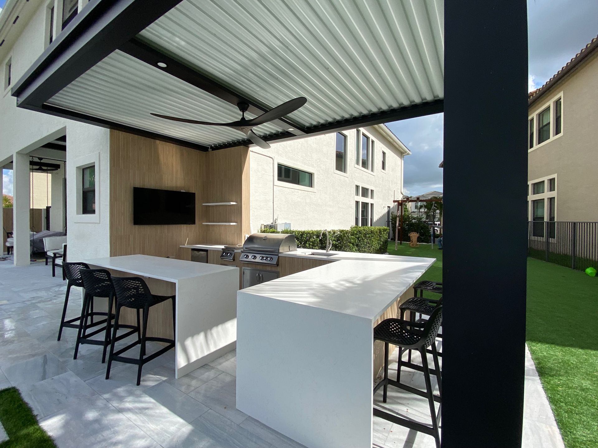 Outdoor kitchen with modern grill and bar seating under a pergola in Lighthouse Point, FL.