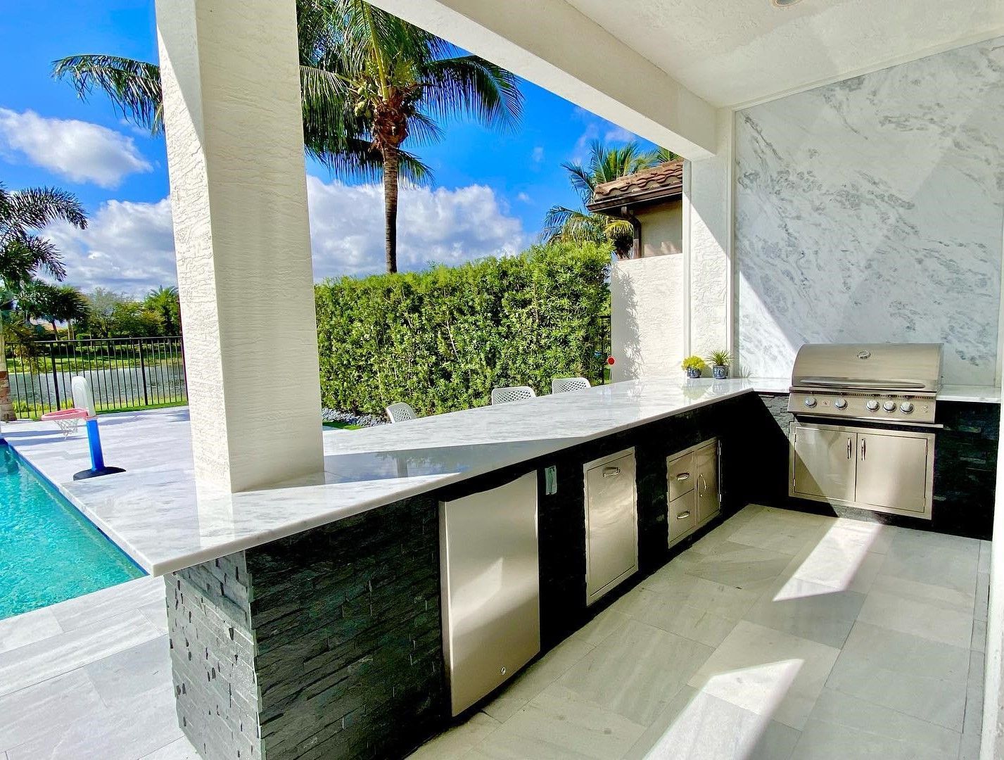 A large outdoor kitchen with a grill and a swimming pool in the background