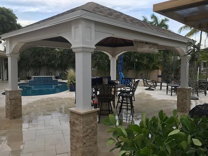 A white gazebo with tables and chairs in front of a pool