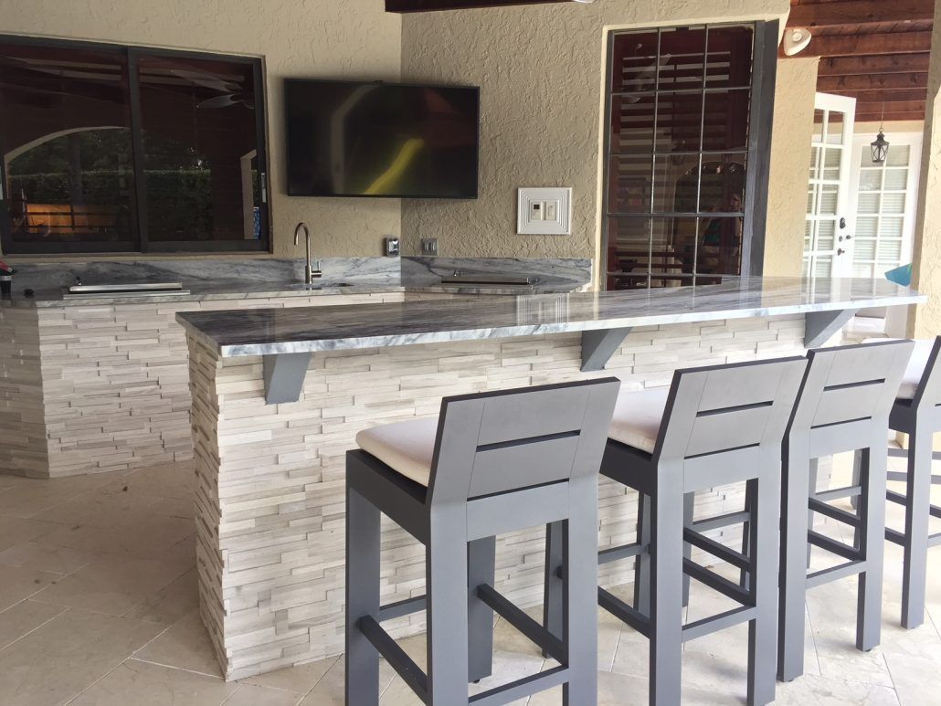 A kitchen with a bar and stools and a flat screen tv