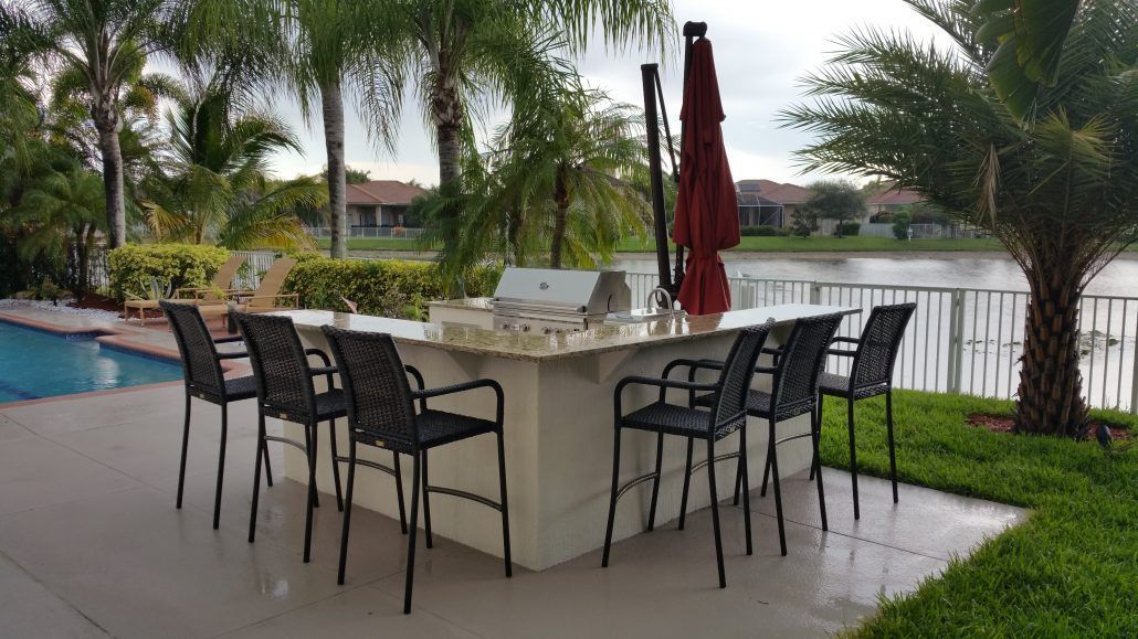 A large outdoor kitchen with a grill and chairs next to a swimming pool.