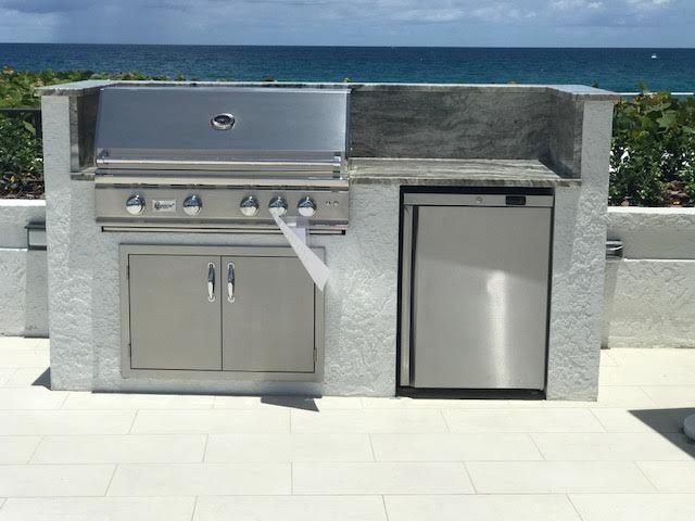 An outdoor kitchen with a grill and a refrigerator with the ocean in the background