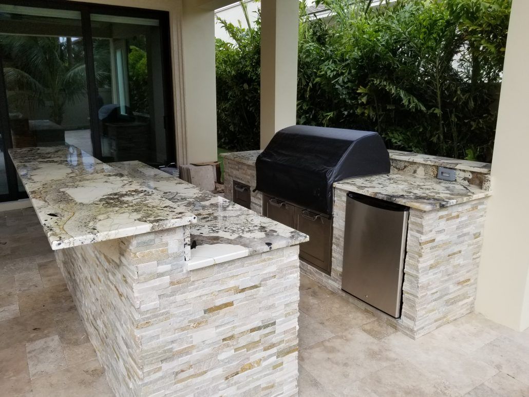 A large outdoor kitchen with granite counter tops and a grill.