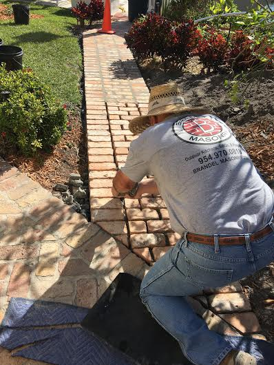 A man wearing a hat is working on a brick walkway.