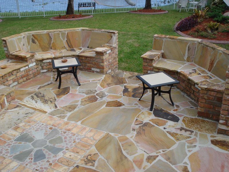 A stone patio with a bench and two tables