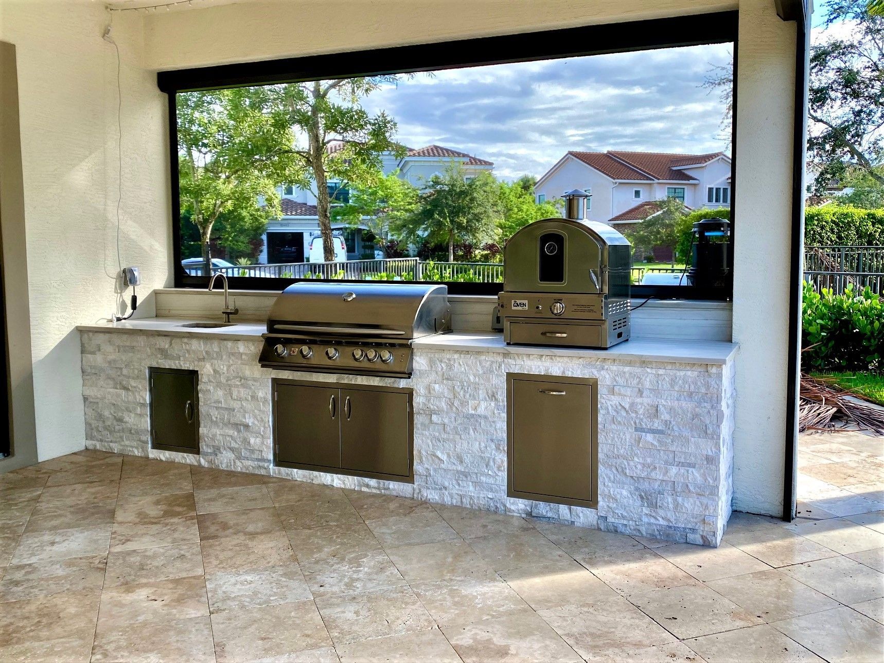 Outdoor kitchen with built-in grill, sink, and pizza oven, set in a landscaped backyard in Lighthouse Point, FL.