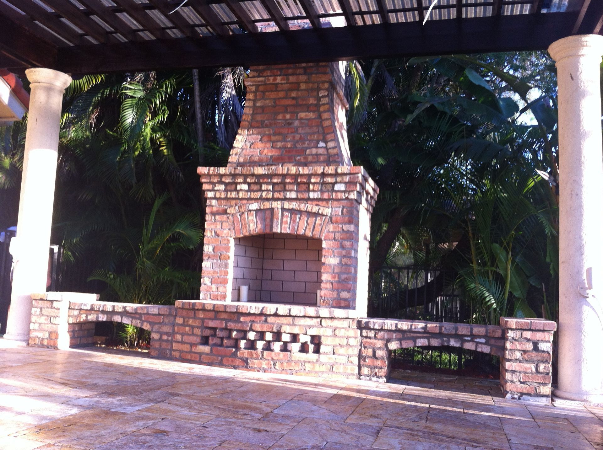 Brick outdoor fireplace with a seating area under a pergola in Boca Raton, FL.