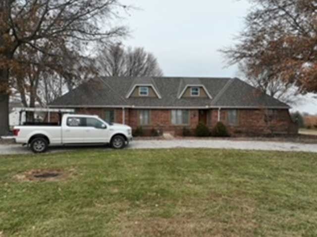 White pickup truck parked in front of a brick ranch-style house with dormers on a cloudy day.