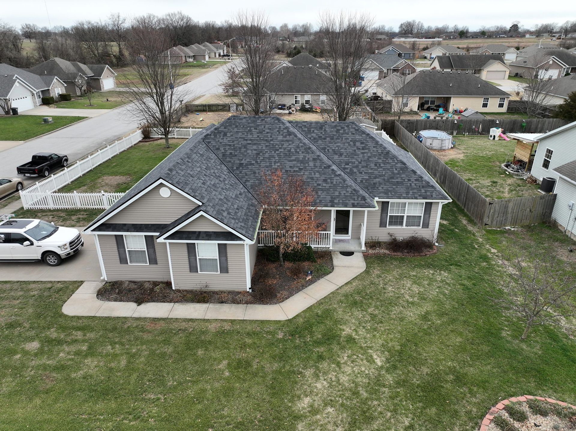 Suburban home with gray roof, tan siding, and green lawn. Driveway with white SUV.