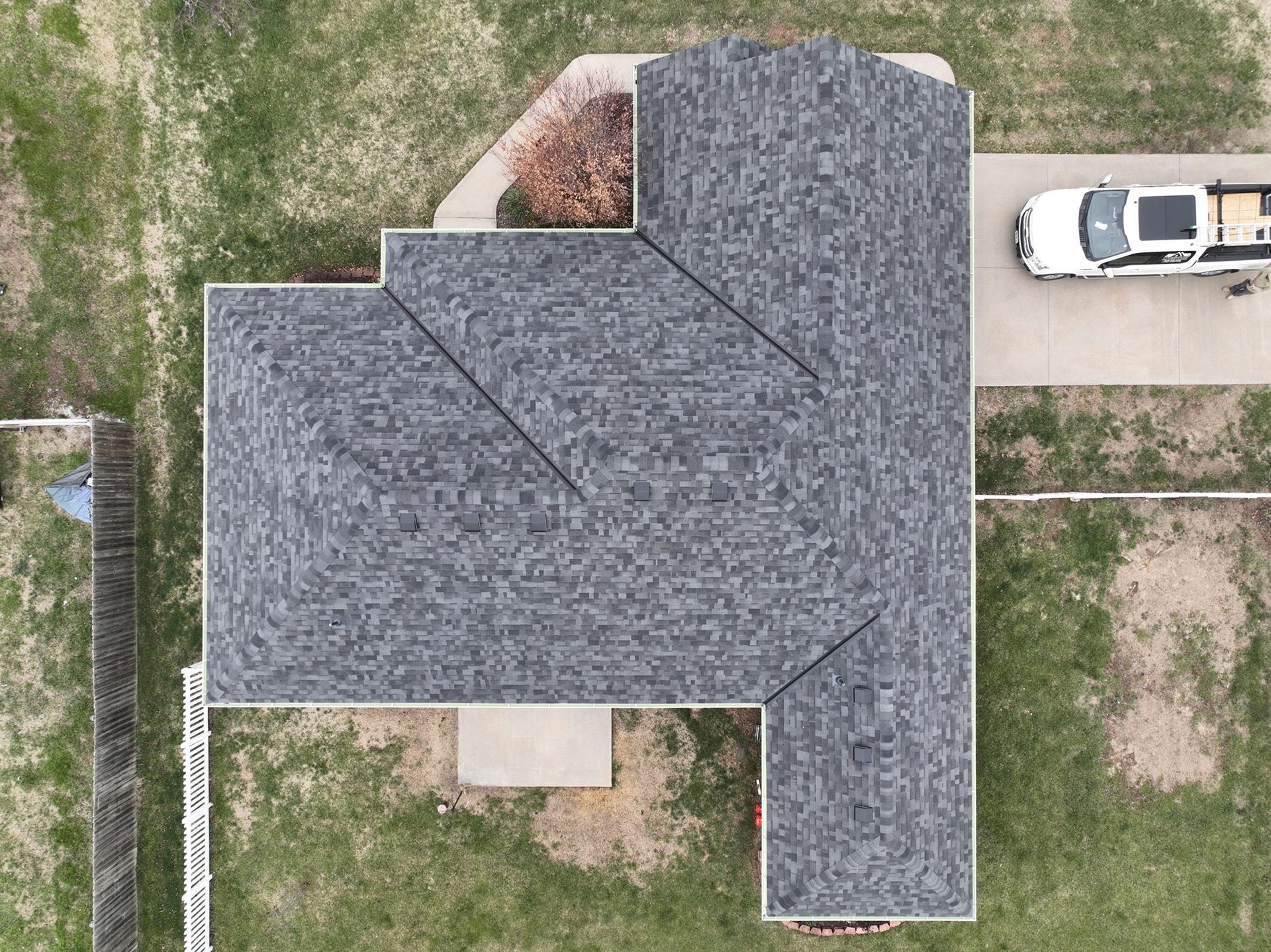 Overhead view of a house with a gray shingled roof, driveway with a white truck, and a grassy yard.