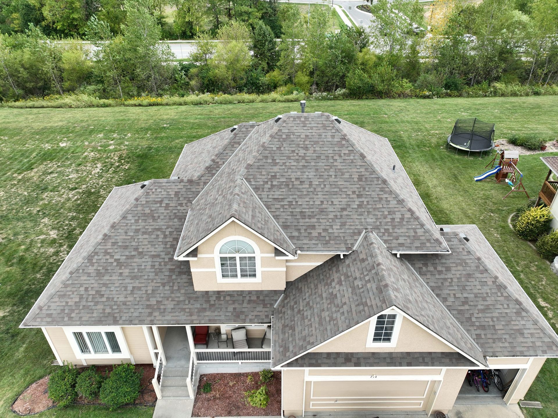 Overhead view of a house with a multi-gabled roof and tan exterior, set on a green lawn.