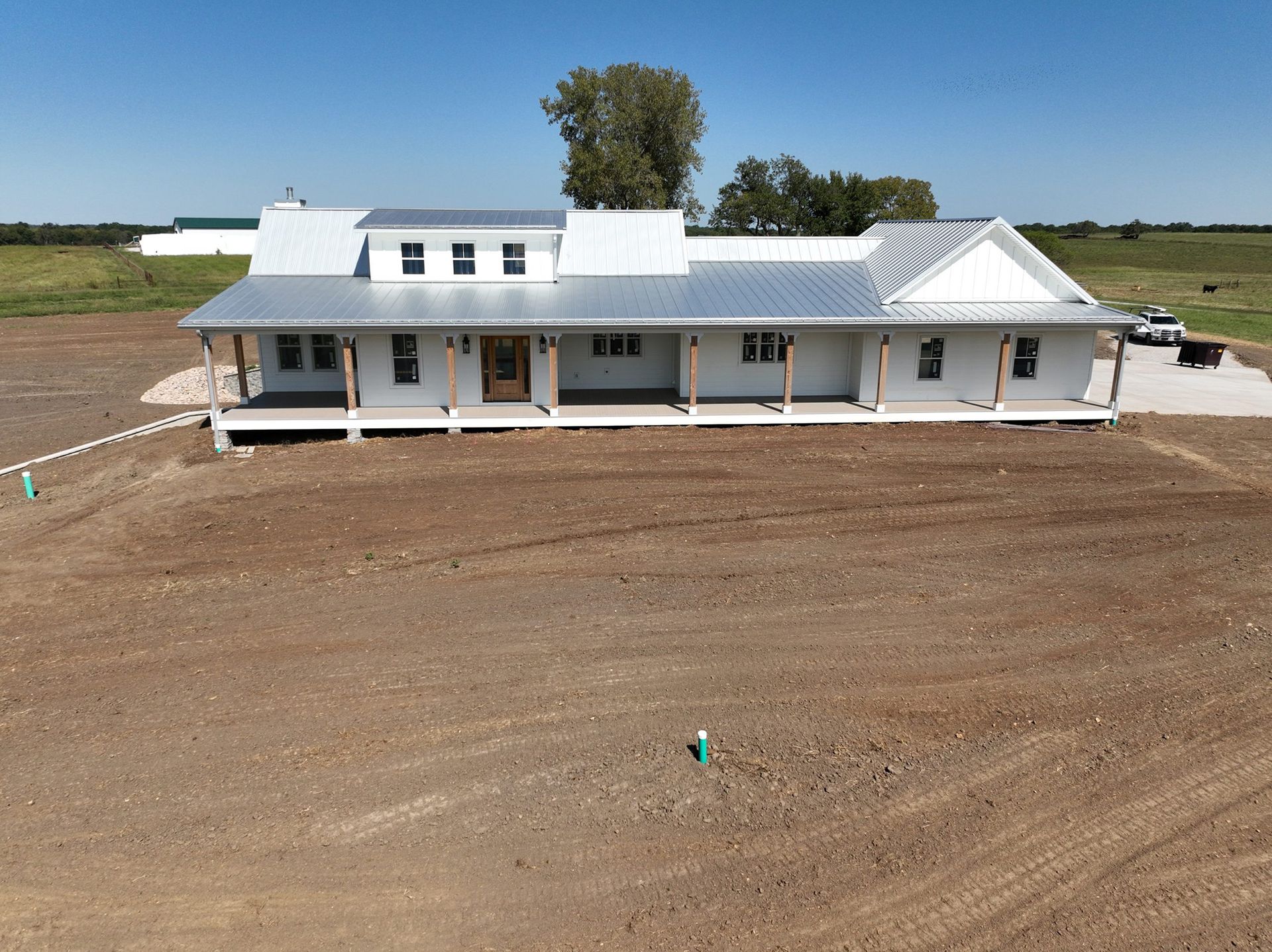 White farmhouse with a long front porch and a metal roof on a sunny day.