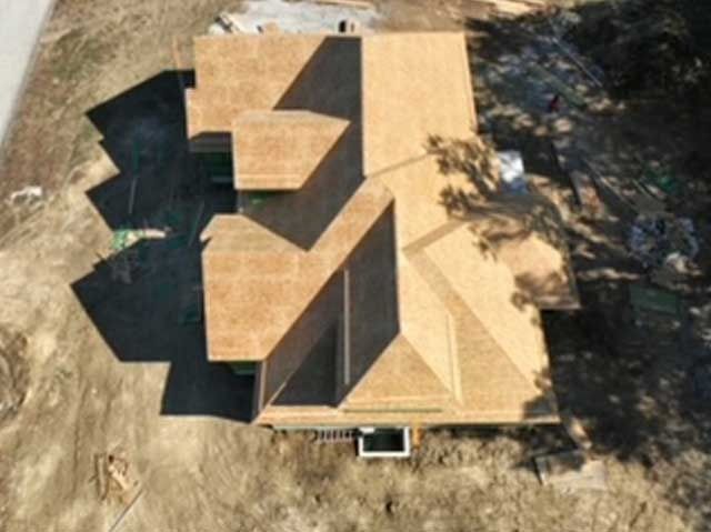Overhead view of a house under construction; brown roof, surrounded by dirt and construction materials.