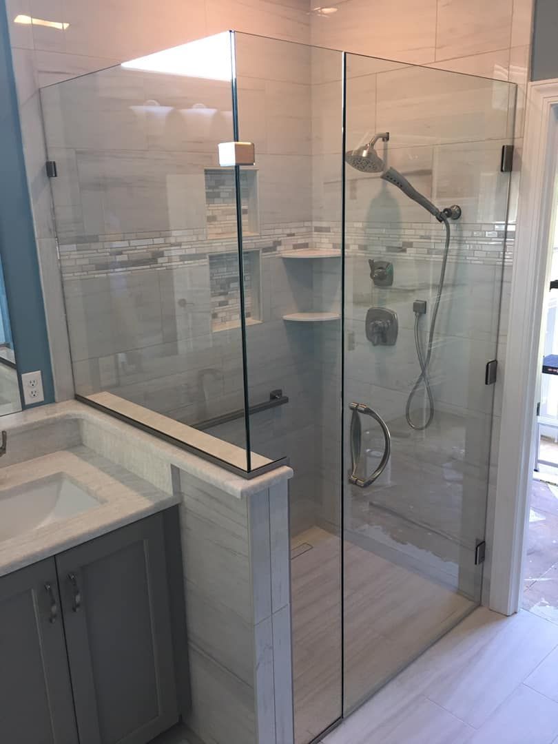 A modern bathroom with a glass shower enclosure and gray vanity. The shower has a handheld showerhead.