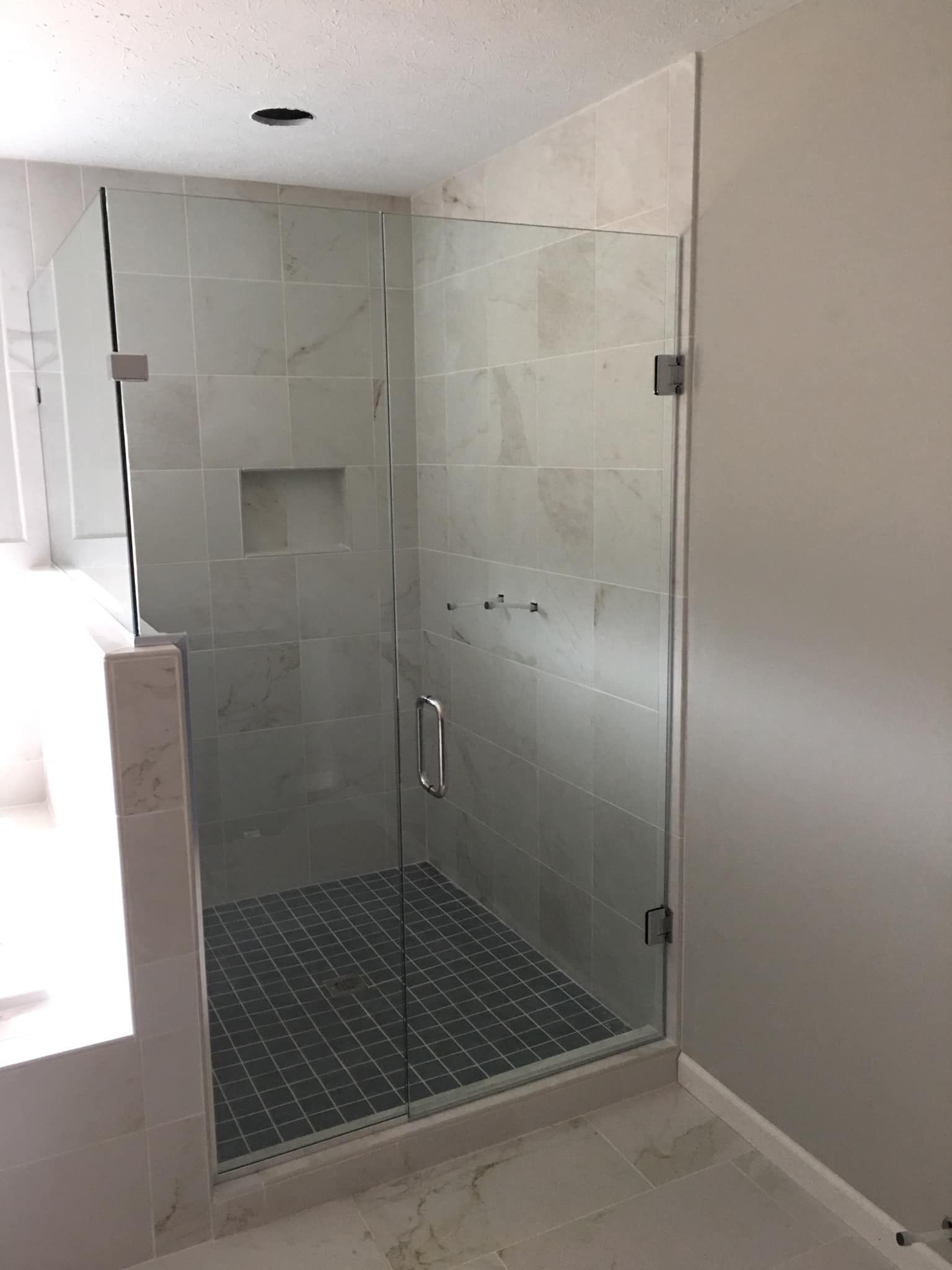 Glass shower enclosure with gray tile walls and floor, stainless steel hardware.