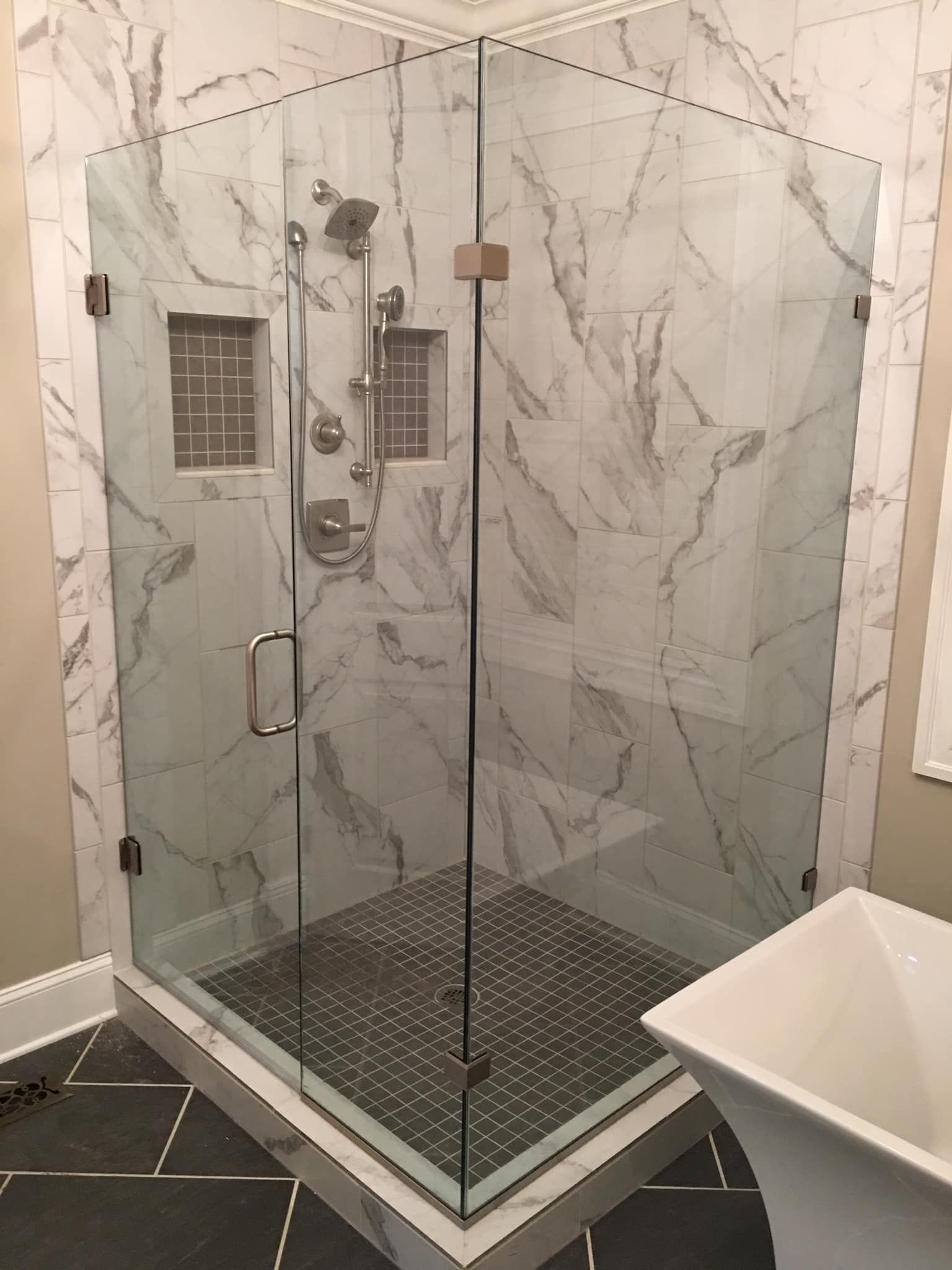 Glass-enclosed shower with white marble-patterned walls and dark gray tiled floor. Includes shower fixtures and door.