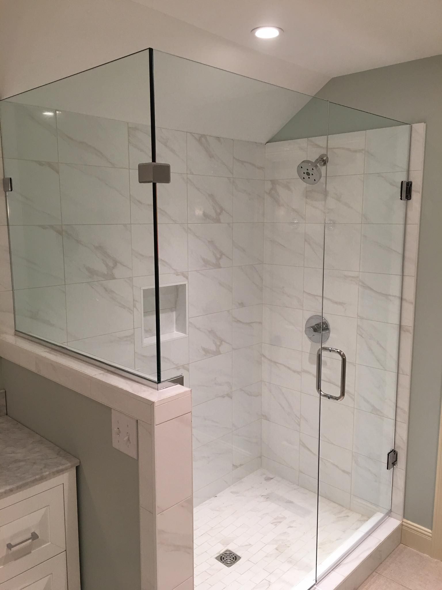 Glass-enclosed shower in a tiled bathroom. A clear glass door and side panel with silver hardware.