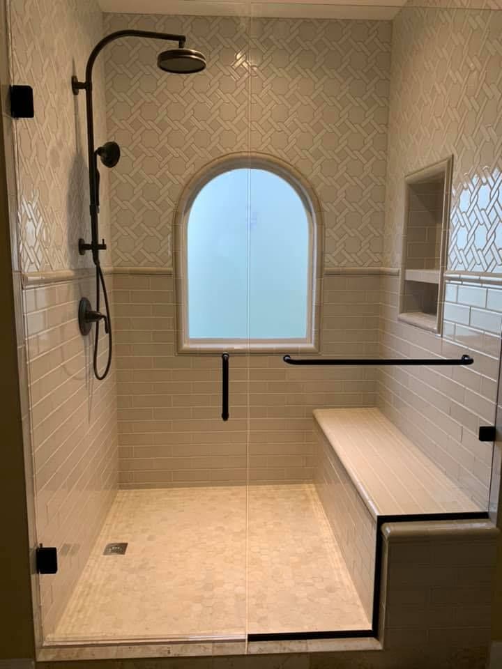 Bathroom with beige tile, arched window, shower bench, and black fixtures.