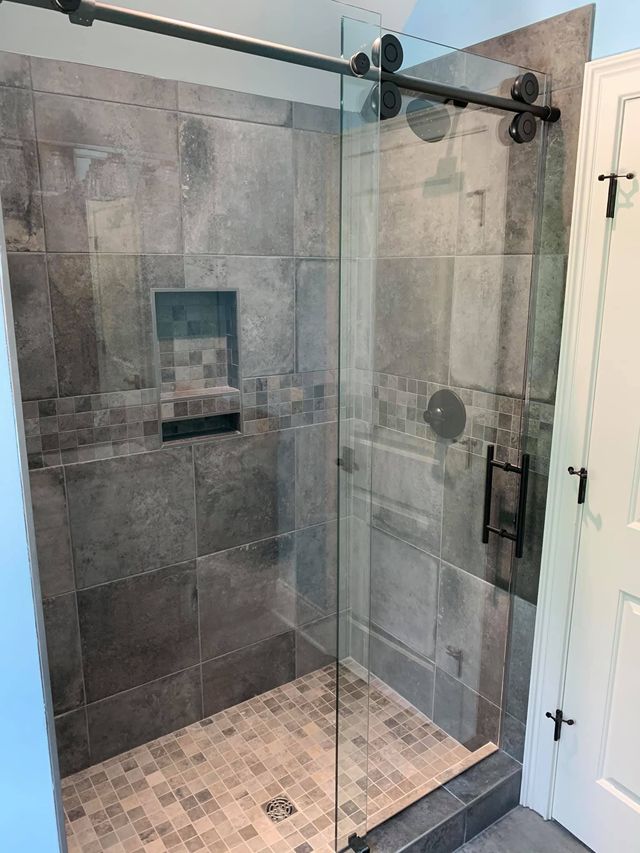 Modern shower with gray tiled walls, glass door, and sliding black hardware.