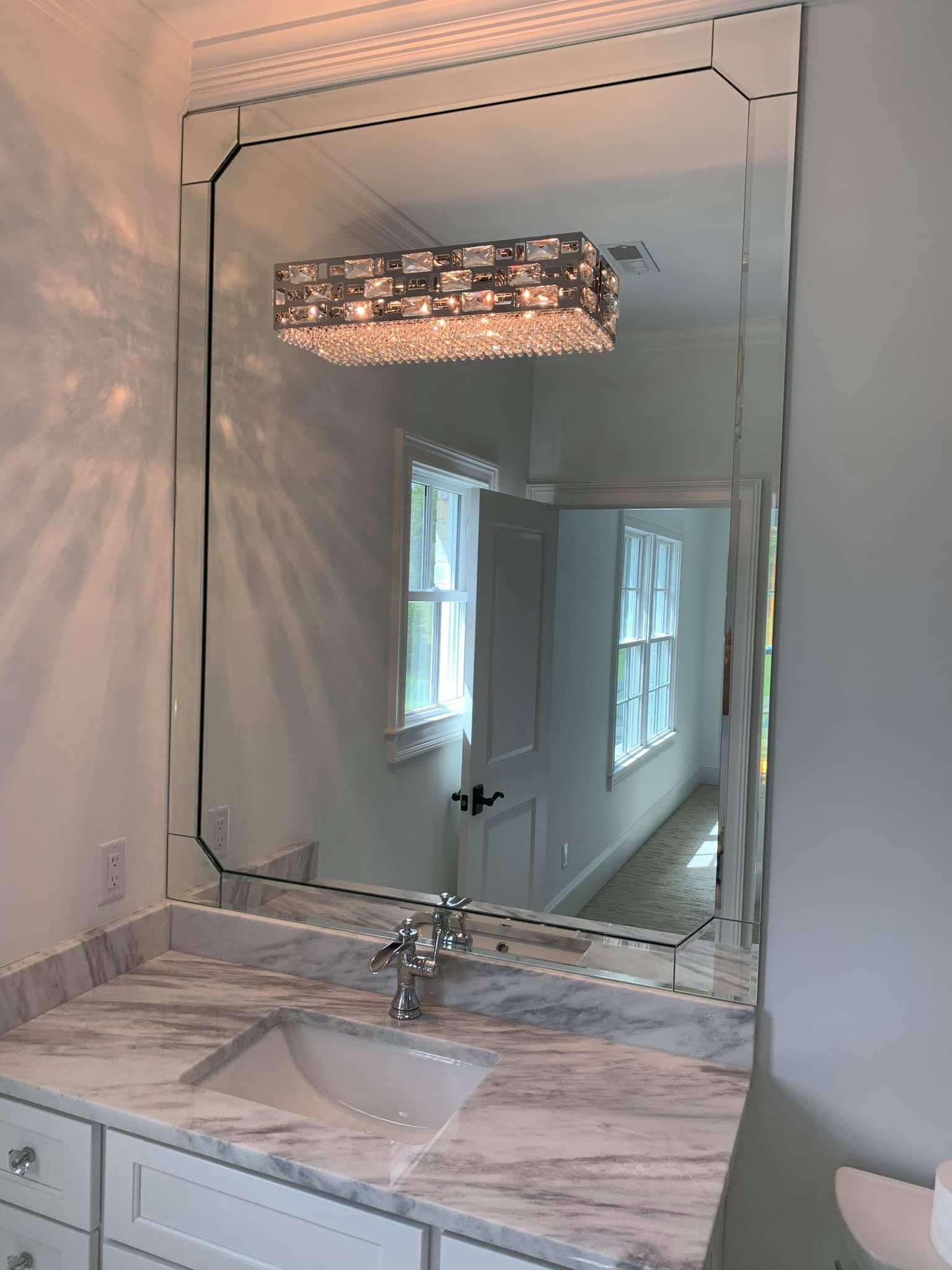 Bathroom with large framed mirror over marble countertop, showing sink, cabinets, and a chandelier.
