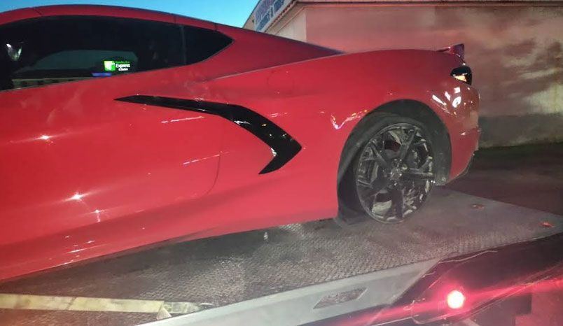 Red Corvette being towed on a flatbed truck; damaged rear tire.
