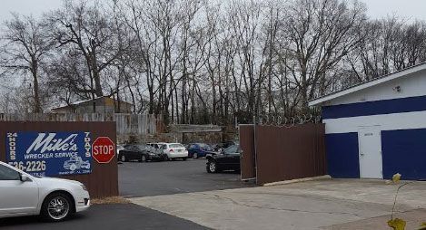 Cars entering and exiting a car repair shop with a blue and white building and brown wall.