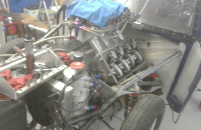 Race car engine and chassis partially assembled, with blue cloth covering some parts.