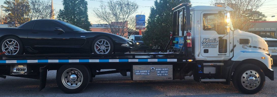 Black sports car on a white tow truck. Setting sun in the background.