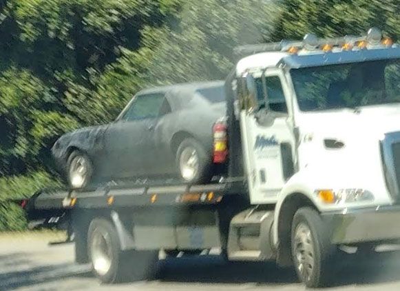 A gray classic car being towed on a flatbed tow truck. The truck is white.