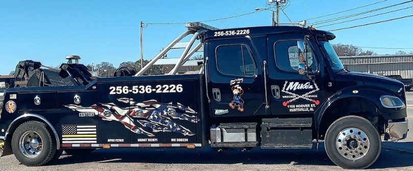 Black tow truck with phone number on the side, parked in front of a building.